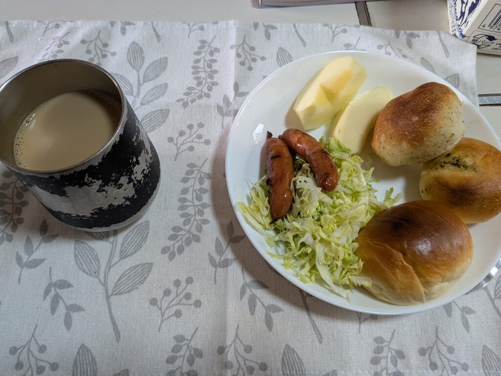37日目 朝食:黒いタンブラーに入ったカフェオレと、白い皿にミニロールパン3個・千切りキャベツのサラダと焼きソーセージ2本・りんごのくし切り2片が並ぶ