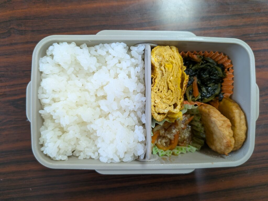 37日目 昼食:弁当箱の左半分を白ご飯が埋め、仕切りの右側に卵焼き・ほうれん草とにんじんの和え物・野菜の煮浸し・チキンナゲット2個が並ぶ