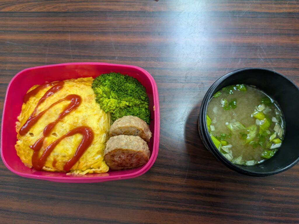 38日目 昼食:ピンクの弁当箱にケチャップをかけたオムライス(卵焼きでご飯を包んだもの)・ブロッコリー・ミニハンバーグ2個が入り、横に青ねぎ入りみそ汁の椀が添えられている