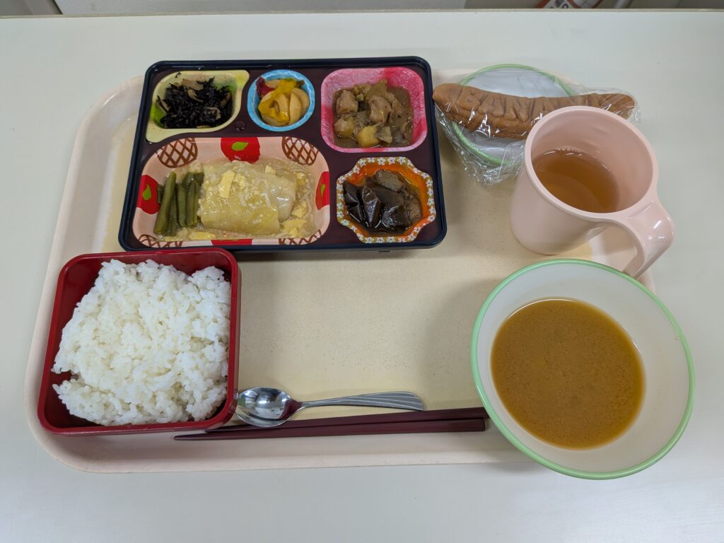 39日目 昼食:左下に白ご飯、右下に味噌汁、中央に仕切り弁当(ロールキャベツ・いんげん・ひじき煮・かぼちゃ煮・鶏肉とさつま芋のマスタード炒め・竹輪のごま炒め)、奥に包まれたバナナと麦茶